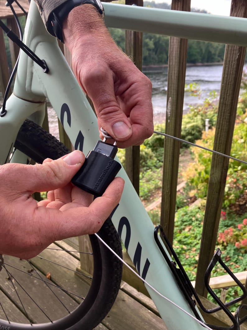 May include: A black bike lock with a silver key attached to a bike frame. The lock is secured to a metal cable.