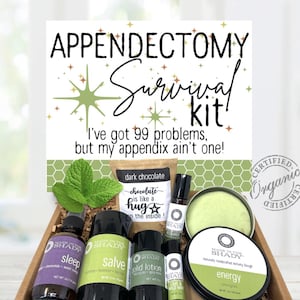 May include: A wooden box filled with self-care items, including bottles, a tin, and a dark chocolate packet. The box is labeled "Appendectomy Survival Kit!" with the text "I've got 99 problems, but my appendix ain't one!"