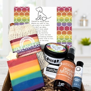 May include: A gift box with a rainbow-colored soap bar, a mesh bag with a rainbow label that reads "LOVE N HUGS", a candle, a spray bottle, and a lip balm. The box also contains a card with a dog illustration and text.