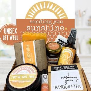 May include: A gift box containing a Sunshine organic citrus soap bar, a jar of raw wildflower honey, a Good Vibes spray, a You've Got This coconut-soy citrus candle, a vanilla rosemary lip balm, and a packet of organic Earl Grey herbal tea.