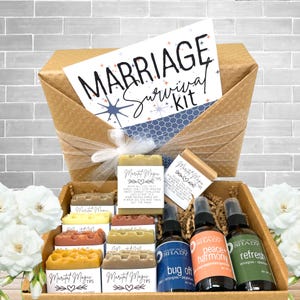 May include: A gift box with a "Marriage Survival Kit" card, soaps, and spray bottles. The box contains various soaps with the text "Maritat Magic Tips". The spray bottles are labeled "bug off", "peace harmony", and "refresh".