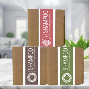 May include: Three rectangular shampoo bars with labels. The labels feature the word "SHAMPOO" and ingredient lists: peppermint, spearmint, tea; cranberry, beets, cocoa; and patchouli, citrus, neem. The bars are brown with white and colored labels.