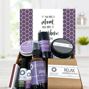 May include: A gift basket with various self-care products, including a sugar scrub, solid lotion, sleep spray, and a bar of soap. The products are in a brown box, with a card that reads "If you are a Mom, you are a superhero."