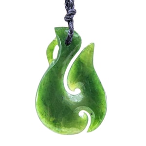May include: A green jade pendant carved in a hook shape, suspended from a black cord. The pendant has a polished, glossy finish and a swirling, organic design. The jade is a rich, deep green color with subtle variations.