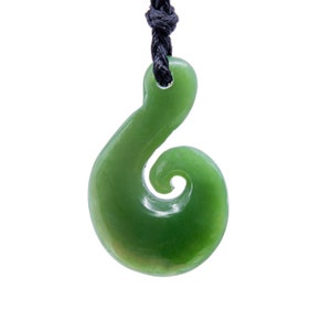 May include: A green jade pendant in a spiral shape, suspended from a black cord. The polished stone has a smooth, glossy finish. The pendant is a traditional Maori design, often worn as a symbol of connection and strength.