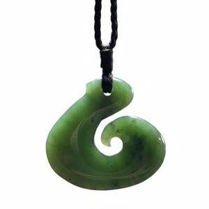 May include: A green jade pendant in a spiral shape, suspended from a black cord. The polished stone has a smooth surface with subtle variations in color. The pendant is a traditional design, often worn as a necklace.