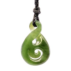 May include: A green jade pendant in a double-twist design, suspended from a black cord. The pendant features a smooth, polished surface with a spiral detail. The necklace is displayed against a white background.
