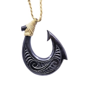 May include: A black wooden fish hook necklace with intricate carvings and a brown rope cord.