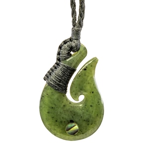 May include: A green jade hook necklace with a black cord. The hook is a traditional Maori design with a small abalone shell inlay.