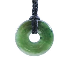 May include: A jade donut pendant with a black woven cord. The pendant is a vibrant green color with lighter green marbling. The pendant has a circular shape with a hole in the center.