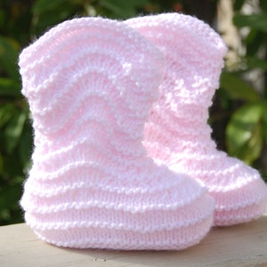 May include: A pair of pink knitted baby booties with a textured pattern.
