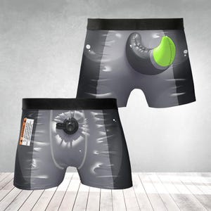 May include: Grey boxer shorts with a black waistband. One pair features a green and black design, while the other has a black circular design. A warning label is visible on one pair.