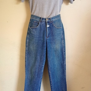 Puede incluir: Un par de pantalones vaqueros azules con una camiseta de manga corta gris claro en un maniquí.