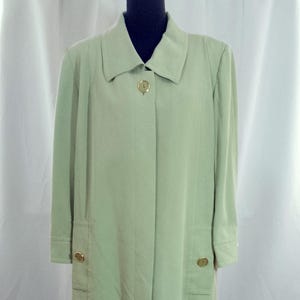 May include: A pale green trench coat with a traditional collar and long sleeves. The coat has gold-coloured buttons and two front pockets. The coat is displayed on a mannequin.