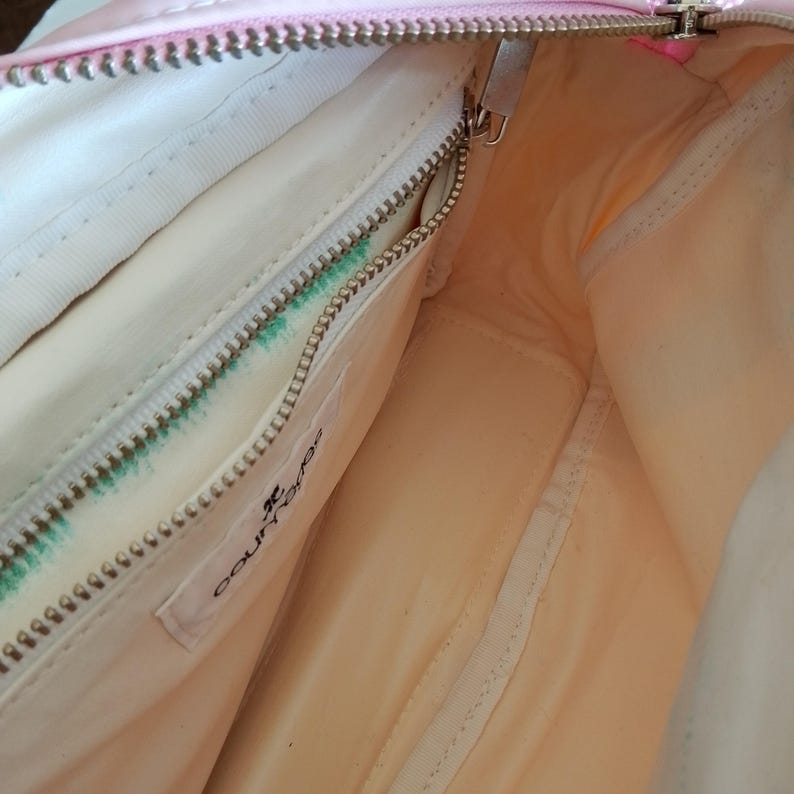 Puede incluir: Vista interior de un bolso de mano rosa y blanco. El bolso tiene un compartimento principal con cremallera y un bolsillo m&aacute;s peque&ntilde;o con cremallera. El forro es de color melocot&oacute;n claro. La cremallera es plateada y el bolso tiene una etiqueta "courr&egrave;ges".