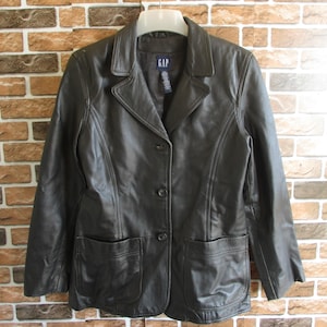 May include: A black leather jacket with a button closure and two front pockets. The jacket has a label that says "GAP" on the front.