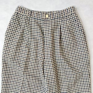 May include: Close-up of a pair of high-waisted pants with a classic black and beige gingham pattern. The pants have a button closure and pleats at the waist. The fabric appears to be a woven material.