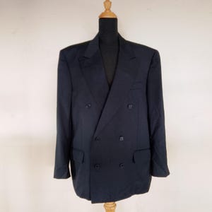 May include: A navy blue double-breasted blazer with six buttons and two front pockets. The blazer is displayed on a wooden mannequin. The jacket has a classic, tailored design.