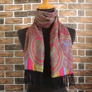 Pode incluir: Um cachecol com padrão paisley e franjas pretas. O cachecol é vermelho, verde, azul e dourado. A etiqueta "PIERRE BALMAIN" é visível no cachecol.