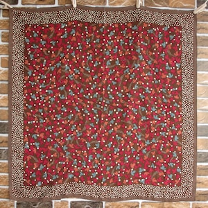 Könnte beinhalten: Ein brauner quadratischer Schal mit einem weißen Punktmuster am Rand. Der Schal hat ein sich wiederholendes Muster aus roten, orangefarbenen und blauen stilisierten Blättern auf braunem Hintergrund.