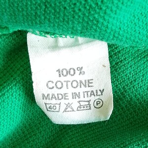 May include: A white clothing tag with black text and symbols, set against a green fabric background. The tag reads "100% COTONE MADE IN ITALY" with care instructions. The fabric appears to be a knitted material.