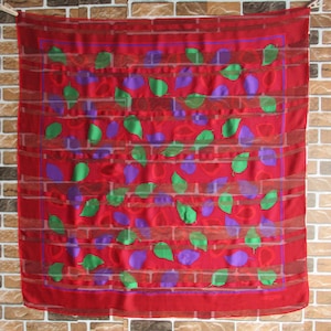 May include: Red silk scarf with a pattern of green and purple leaves. The scarf has a checkered border.