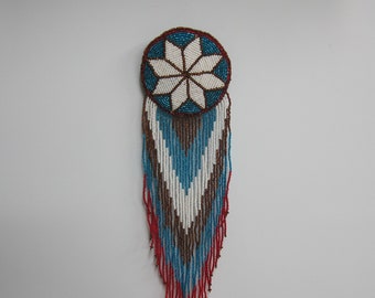 May include: A beaded Native American dreamcatcher with a white starburst design in the center, surrounded by blue and brown beads. The dreamcatcher has a long fringe of red, white, blue, and brown beads.
