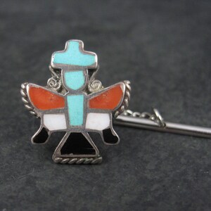 May include: A silver tie tack with a turquoise, red, white, and black geometric design. The tie tack has a chain attached to a silver bar.