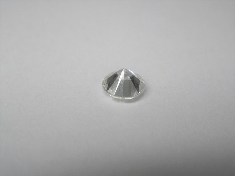 May include: A clear round diamond gemstone with a pointed top.