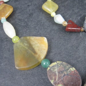 May include: A multi-colored gemstone necklace with various shapes and sizes of beads. The necklace features green, yellow, brown, red, and white beads.