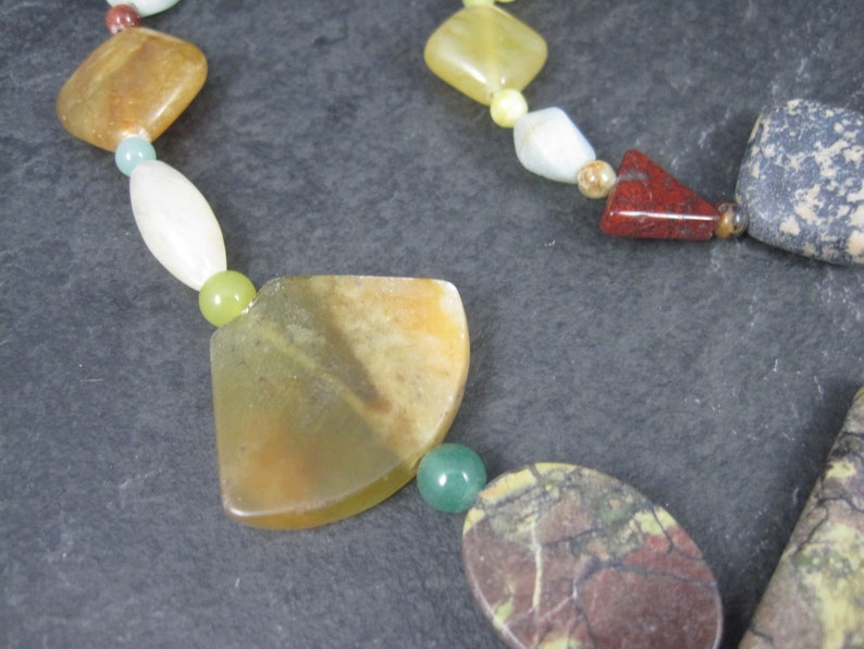 May include: A multi-colored gemstone necklace with various shapes and sizes of beads. The necklace features green, yellow, brown, red, and white beads.