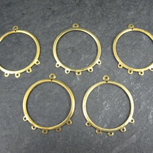 Puede incluir: Cinco componentes de pendientes de aro de metal color lat&oacute;n. Cada aro tiene un peque&ntilde;o lazo en la parte superior y seis lazos m&aacute;s peque&ntilde;os en la parte inferior. Los aros est&aacute;n dispuestos sobre una superficie gris oscuro.