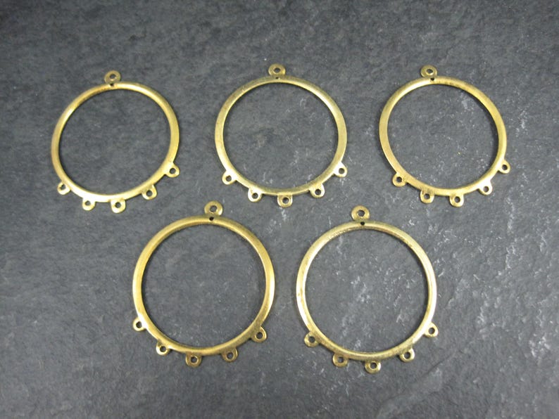 Puede incluir: Cinco componentes de pendientes de aro de metal color lat&oacute;n. Cada aro tiene un peque&ntilde;o lazo en la parte superior y seis lazos m&aacute;s peque&ntilde;os en la parte inferior. Los aros est&aacute;n dispuestos sobre una superficie gris oscuro.