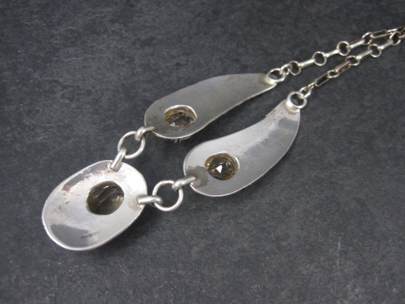 May include: Silver necklace with two teardrop-shaped pendants, each featuring a clear gemstone. The necklace has a delicate chain.