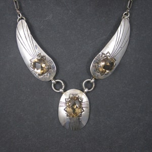May include: A silver necklace with three teardrop-shaped pendants, each featuring a faceted brown gemstone. The pendants are connected by silver chains.