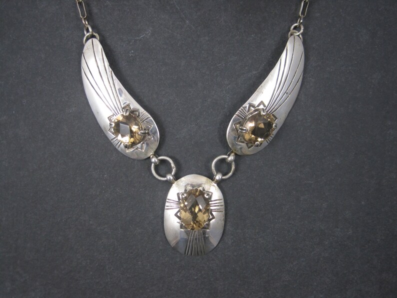 May include: A silver necklace with three teardrop-shaped pendants, each featuring a faceted brown gemstone. The pendants are connected by silver chains.