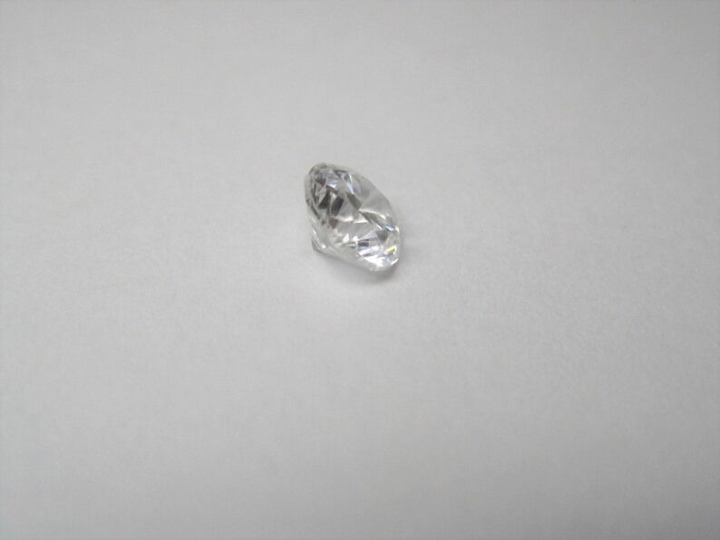 May include: A clear, oval-shaped diamond gemstone on a white background.