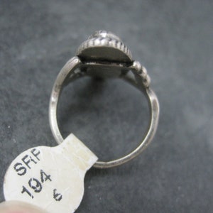 May include: A silver ring with a teardrop-shaped setting. The setting is adorned with small, round embellishments. The ring band is simple and smooth. A price tag is attached to the ring.