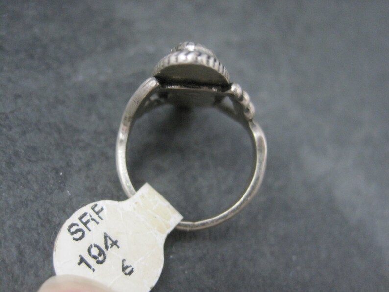 May include: A silver ring with a teardrop-shaped setting. The setting is adorned with small, round embellishments. The ring band is simple and smooth. A price tag is attached to the ring.