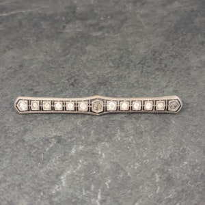 May include: A silver bar brooch with a black enamel design and a row of clear stones.