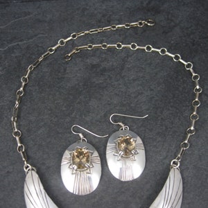 May include: A silver necklace and earrings set with a crescent moon pendant and oval shaped earrings with a brown gemstone in the center.