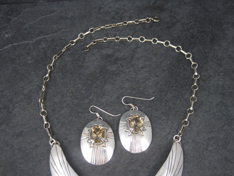 May include: A silver necklace and earrings set with a crescent moon pendant and oval shaped earrings with a brown gemstone in the center.