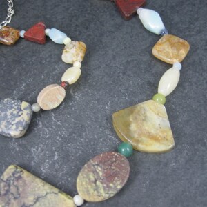 May include: A multi-colored gemstone necklace with a variety of shapes and sizes. The necklace features brown, red, green, white, and beige stones.