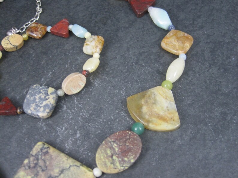 May include: A multi-colored gemstone necklace with a variety of shapes and sizes. The necklace features brown, red, green, white, and beige stones.