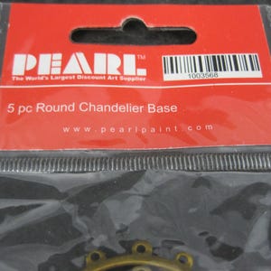 Puede incluir: Un paquete que contiene cinco bases redondas para candelabros. La etiqueta roja dice "PEARL" y "The World's Largest Discount Art Supplier". El texto "5 pc Round Chandelier Base" tambi&eacute;n es visible. Un c&oacute;digo de barras y la direcci&oacute;n del sitio web tambi&eacute;n est&aacute;n presentes.