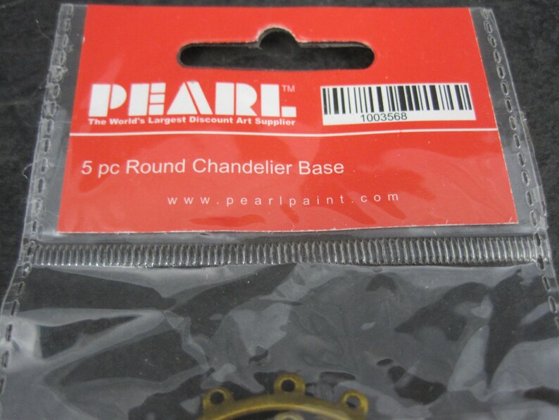 Puede incluir: Un paquete que contiene cinco bases redondas para candelabros. La etiqueta roja dice "PEARL" y "The World's Largest Discount Art Supplier". El texto "5 pc Round Chandelier Base" tambi&eacute;n es visible. Un c&oacute;digo de barras y la direcci&oacute;n del sitio web tambi&eacute;n est&aacute;n presentes.