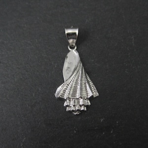May include: A silver pendant in the shape of a stylized seashell. The pendant has a loop at the top for a chain and features detailed ridges and textures. The design is symmetrical and has a polished finish.