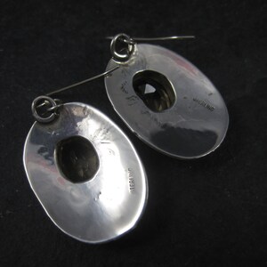 May include: A pair of silver earrings with a round, open design. The earrings are marked "STERLING" on the back.