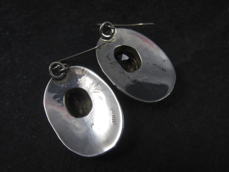May include: A pair of silver earrings with a round, open design. The earrings are marked "STERLING" on the back.