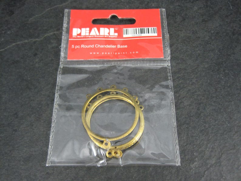 Puede incluir: Un paquete que contiene cinco bases redondas para candelabros. Las bases son de metal color oro y est&aacute;n en una bolsa de pl&aacute;stico transparente. El paquete tiene una etiqueta roja con la marca "PEARL".